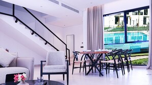 A modern living room with a staircase, a dining area with a pool view, and a sofa with decorative pillows. - Hafawah Resort (Madinah)