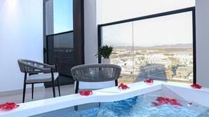 Ein moderner Balkon mit Blick auf eine Stadtlandschaft, zwei Korbstühle, ein kleiner Topfpflanze und ein Pool mit Rosenblüten.