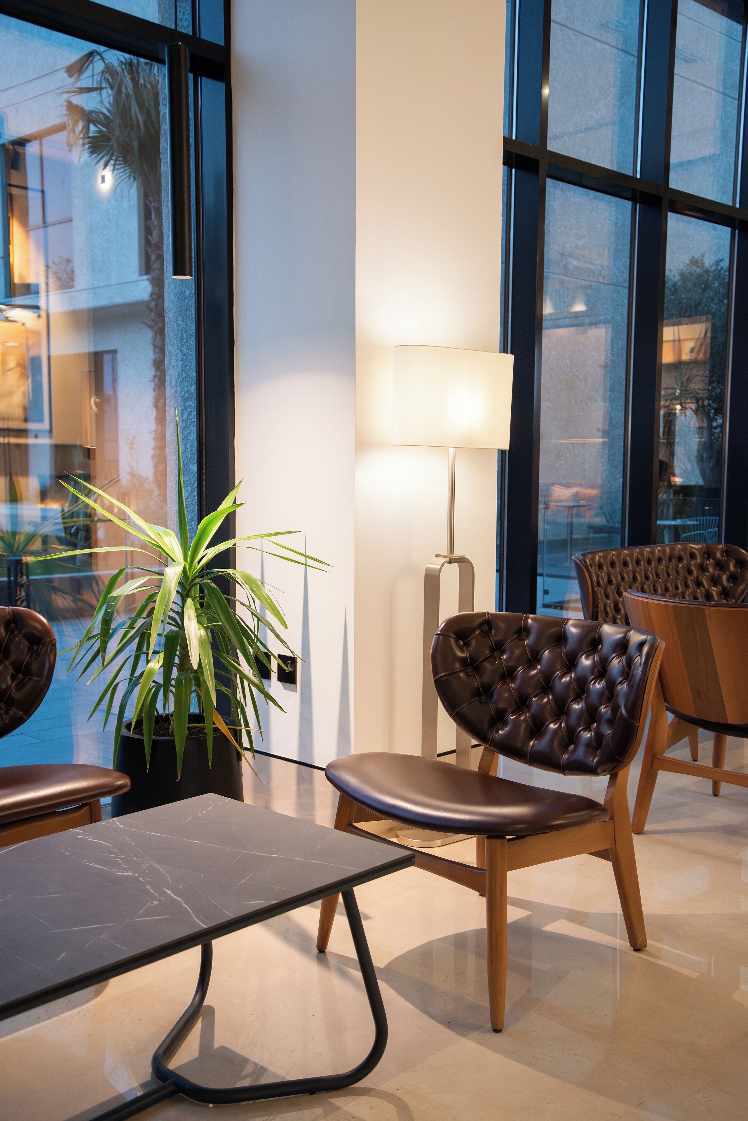 A modern indoor seating area with a glass wall, a potted plant, and a lamp.