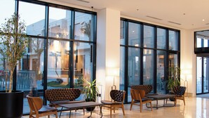 Eine großzügige Lobby mit großen Fenstern, einer Sitzecke mit Stühlen und einer Bank, sowie einer Zimmerpflanze.