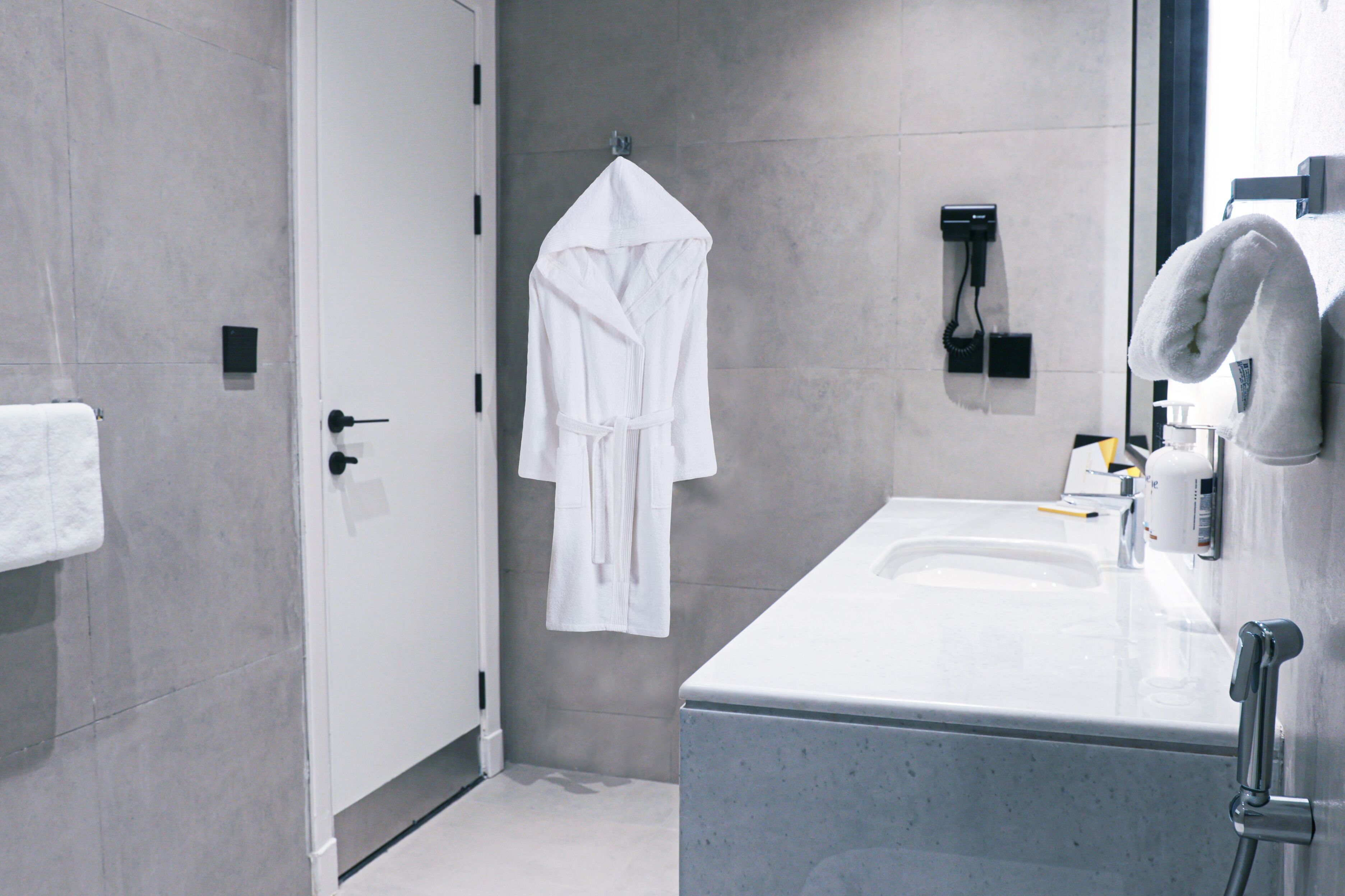 A modern bathroom with a white sink, a mirror, a towel rack, and a robe hanging on the wall.
