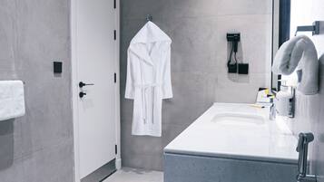 A modern bathroom with a white sink, a mirror, a towel rack, and a robe hanging on the wall.