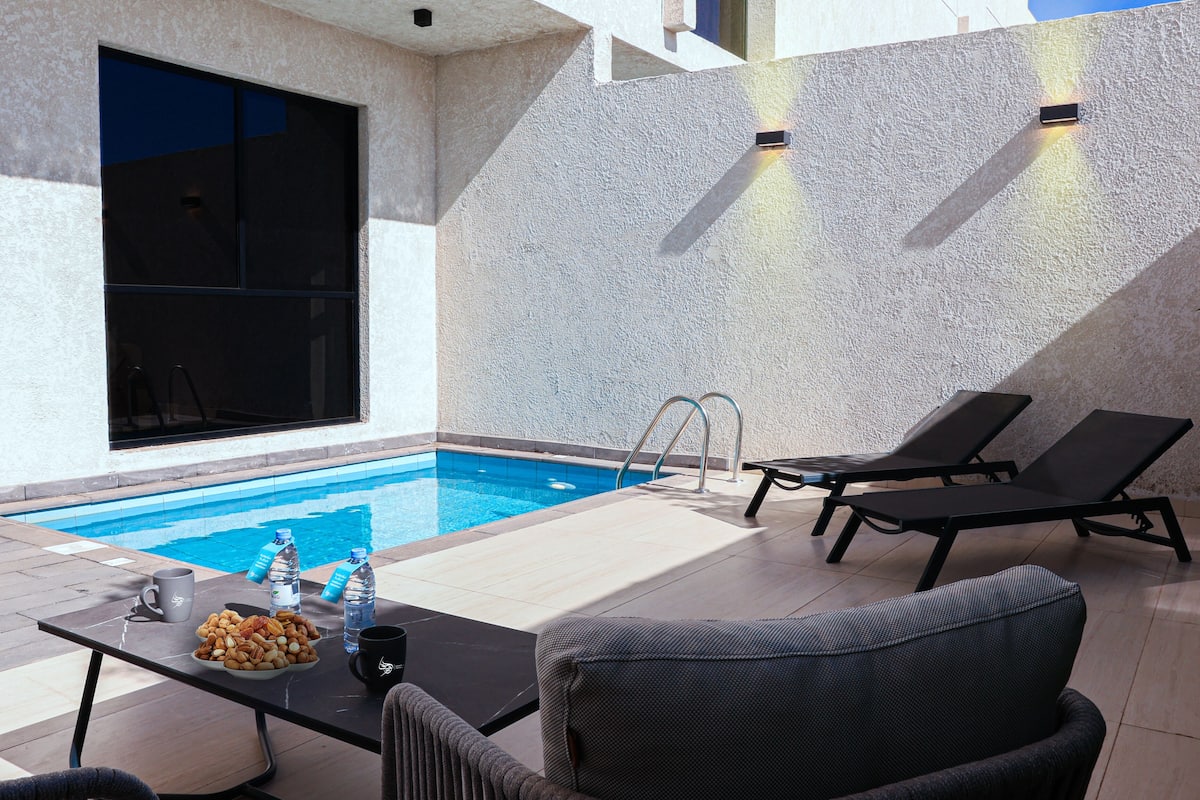 A poolside area with a table set with snacks and drinks, lounge chairs, and a clear view of the pool.