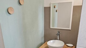 Une salle de bain avec un meuble-lavabo en bois, un lavabo blanc, un miroir et deux paniers placés sous le meuble-lavabo.