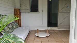 Une petite terrasse avec un canapé blanc, une table ronde et une porte en bois.