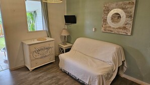 Une chambre avec un lit recouvert d’une couverture blanche, une commode au design vintage, un téléviseur fixé au mur et une œuvre d’art circulaire originale.