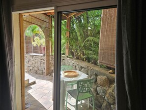 A patio with a table and chairs, a stone wall, and a view of lush greenery.