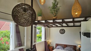 Une chambre à coucher avec un lit, des tables de chevet, un luminaire suspendu et une vue sur la verdure à l’extérieur.