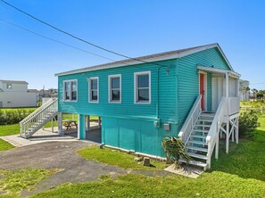A turquoise two-story house with a red door, a front porch, and a staircase leading to the second floor.