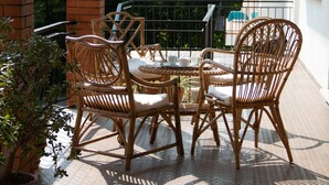 A patio with wicker furniture and a tiled floor, surrounded by greenery and a brick wall.