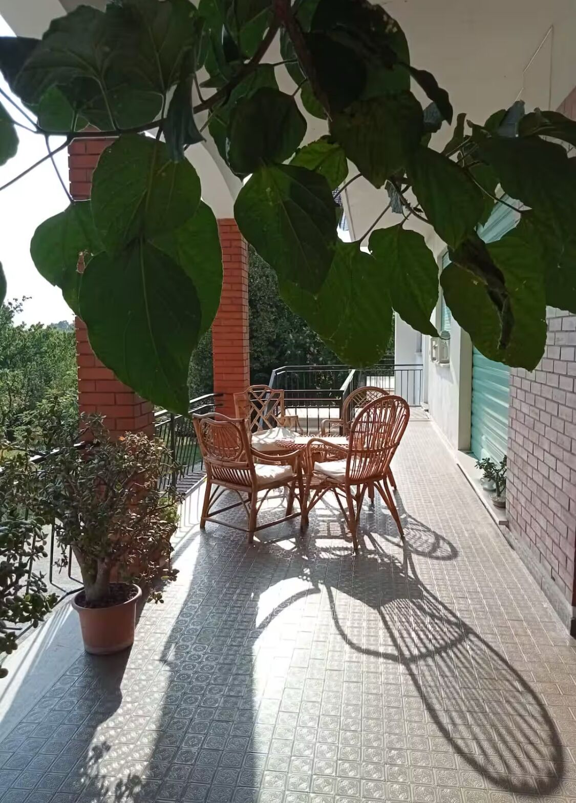 En overdækket terrasse med borde og stole, omgivet af krukker med planter og en murstensmur.
