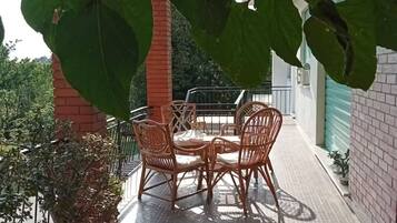 En overdækket terrasse med borde og stole, omgivet af krukker med planter og en murstensmur.
