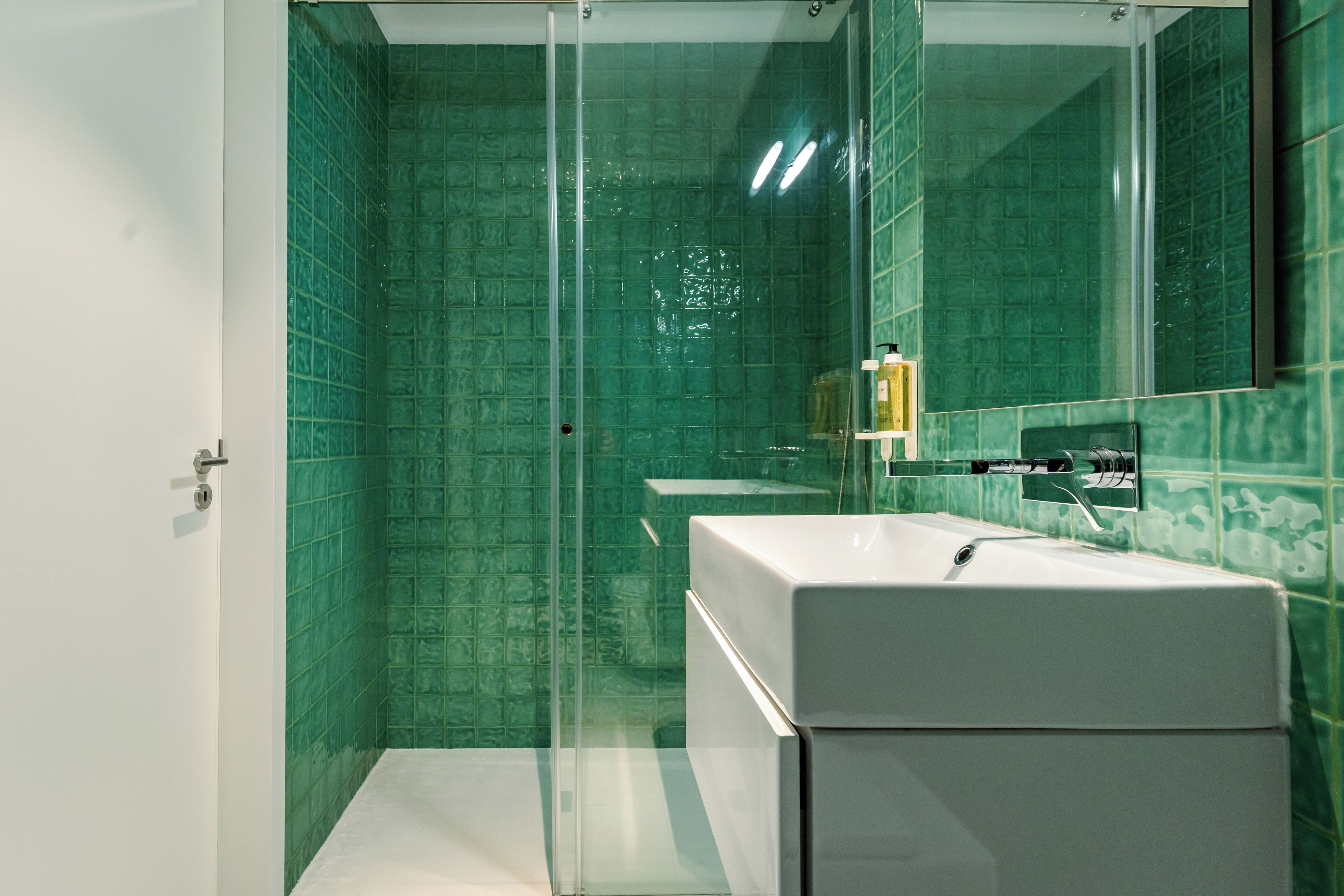 A bathroom with a glass shower enclosure, a white sink, and a mirror.