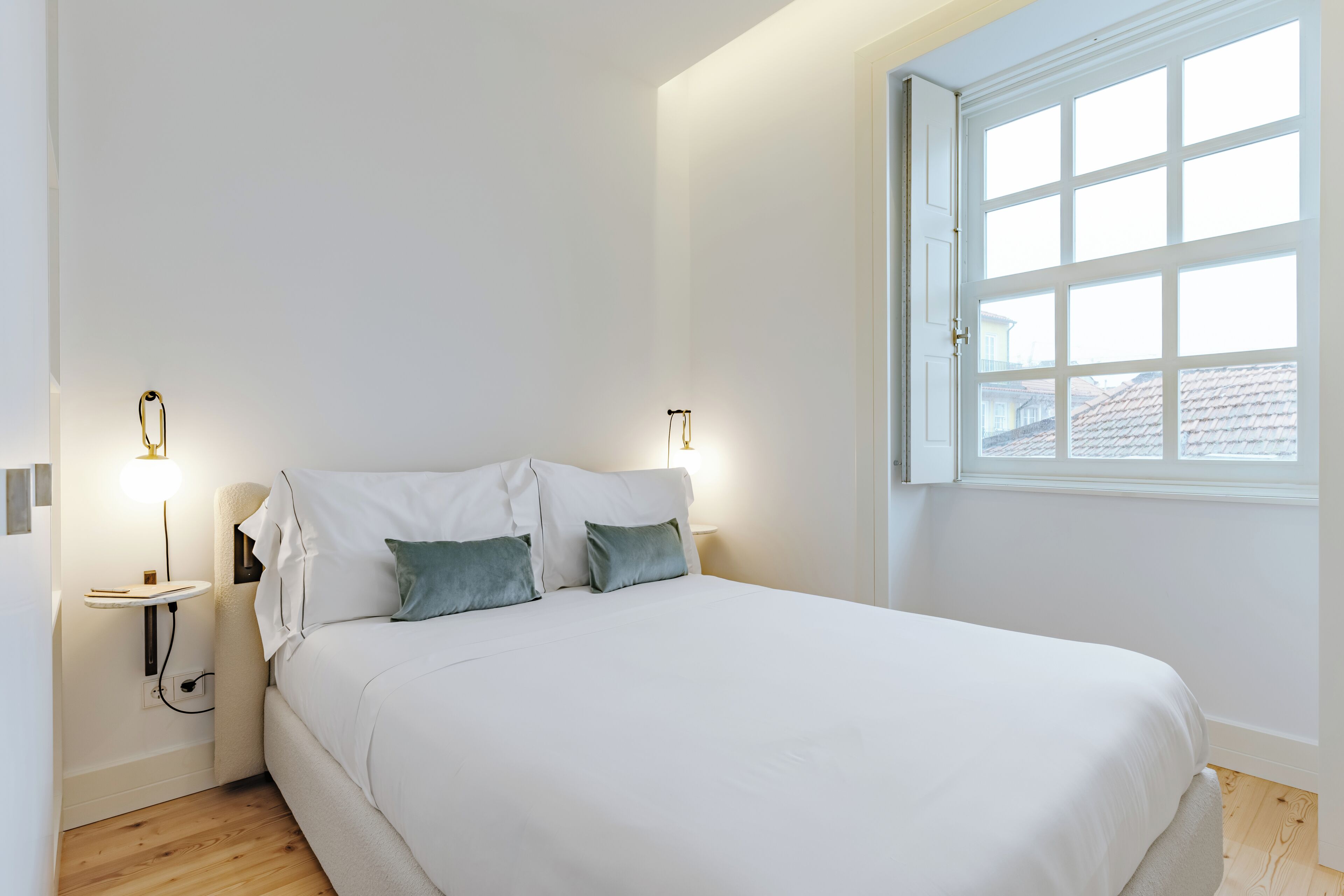 A bedroom with a large bed, two bedside tables, and a window with a view of a house.