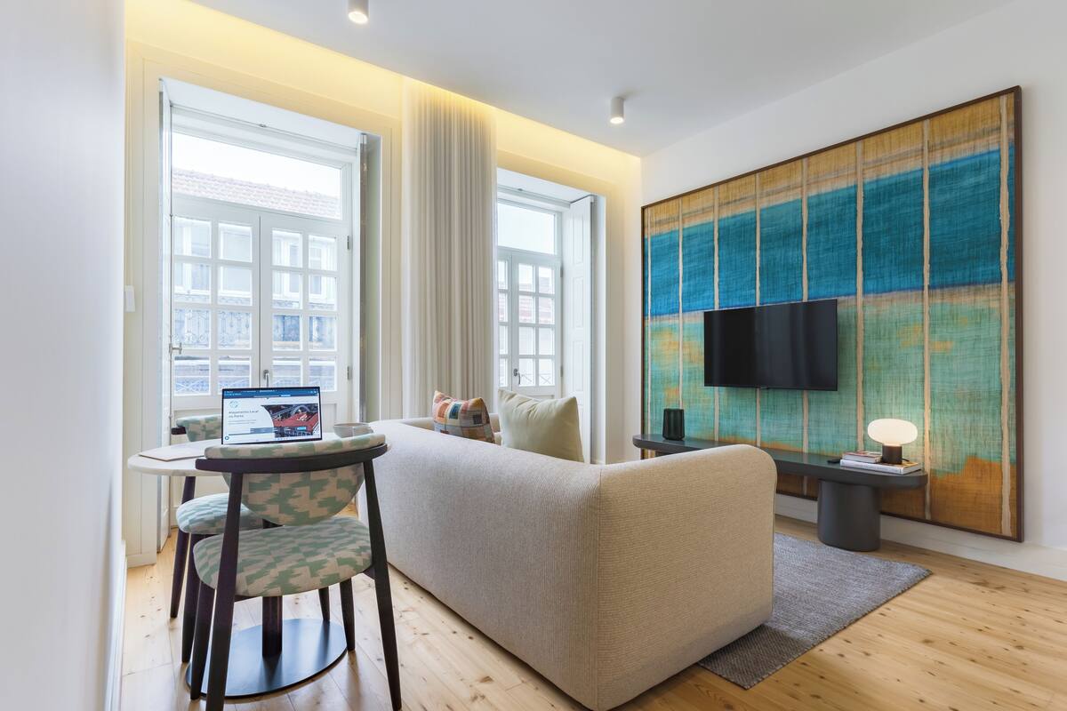 A modern living room with a sofa, a small table, a chair, and a TV mounted on the wall.