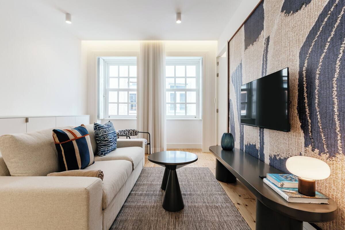 A modern living room with a sofa, a coffee table, a flat-screen TV mounted on the wall, and a large abstract painting.
