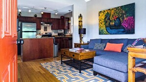 A modern kitchen with wooden cabinets, a central island, and a dining area with a blue sofa and patterned rug. - Feels Like Home - Close to Downtown! (Raleigh)