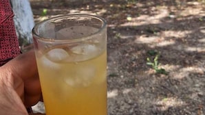 A person holding a glass of iced beverage outdoors with trees and a vehicle in the background. - Casa Donjá (Serro)
