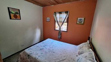 Um quarto pequeno com uma cama de solteiro, uma janela com cortina e duas decorações na parede.