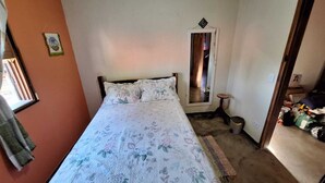 A bedroom with a bed, a small stool, a trash bin, and a mirror on the wall. - Casa Donjá (Serro)