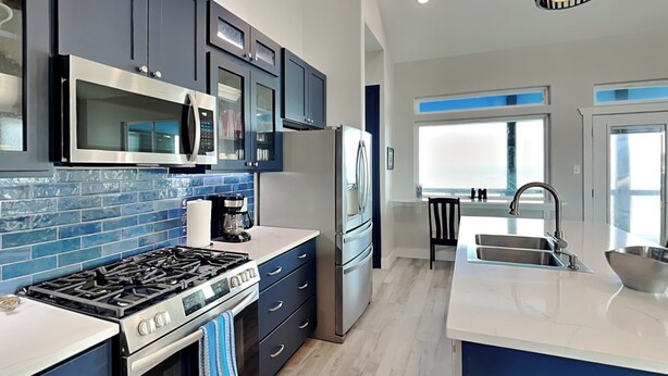 A modern kitchen with dark blue cabinets, stainless steel appliances, and a large island with a sink. - Heron House | Pet-friendly with Private Pool (Rockport)