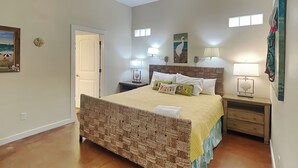 A bedroom with a bed, two bedside tables, a ceiling fan, and a painting on the wall. - Jamaica Me Happy | Charming Coastal Getaway (Port Aransas)