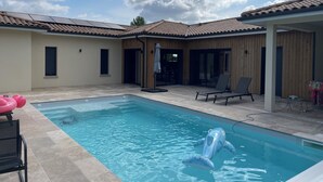 En swimmingpool med en blå oppustelig hval, liggestole og en overdækket terrasse.