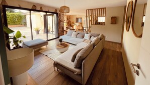 En rummelig stue med en stor sofa, et spiseområde og udsigt til en have gennem store vinduer.