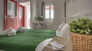 A hotel room with a bed, a desk, a chair, a window, and a basket of greenery. - Arodou Studio Mykonos (Mykonos)