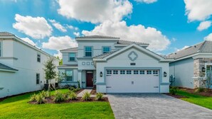 A two-story house with a garage, surrounded by a well-maintained lawn and a clear sky. - South-Facing Pool & Spa • Game Room • Conservation View • Near Disney (Four Corners)