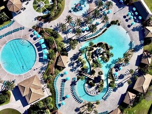 Vue aĂ©rienne dâun complexe hĂŽtelier dotĂ© de plusieurs piscines, de chaises longues et de palmiers.