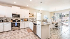 A modern kitchen with white cabinets, stainless steel appliances, and a granite countertop. - South-Facing Pool & Spa • Game Room • Conservation View • Near Disney (Four Corners)
