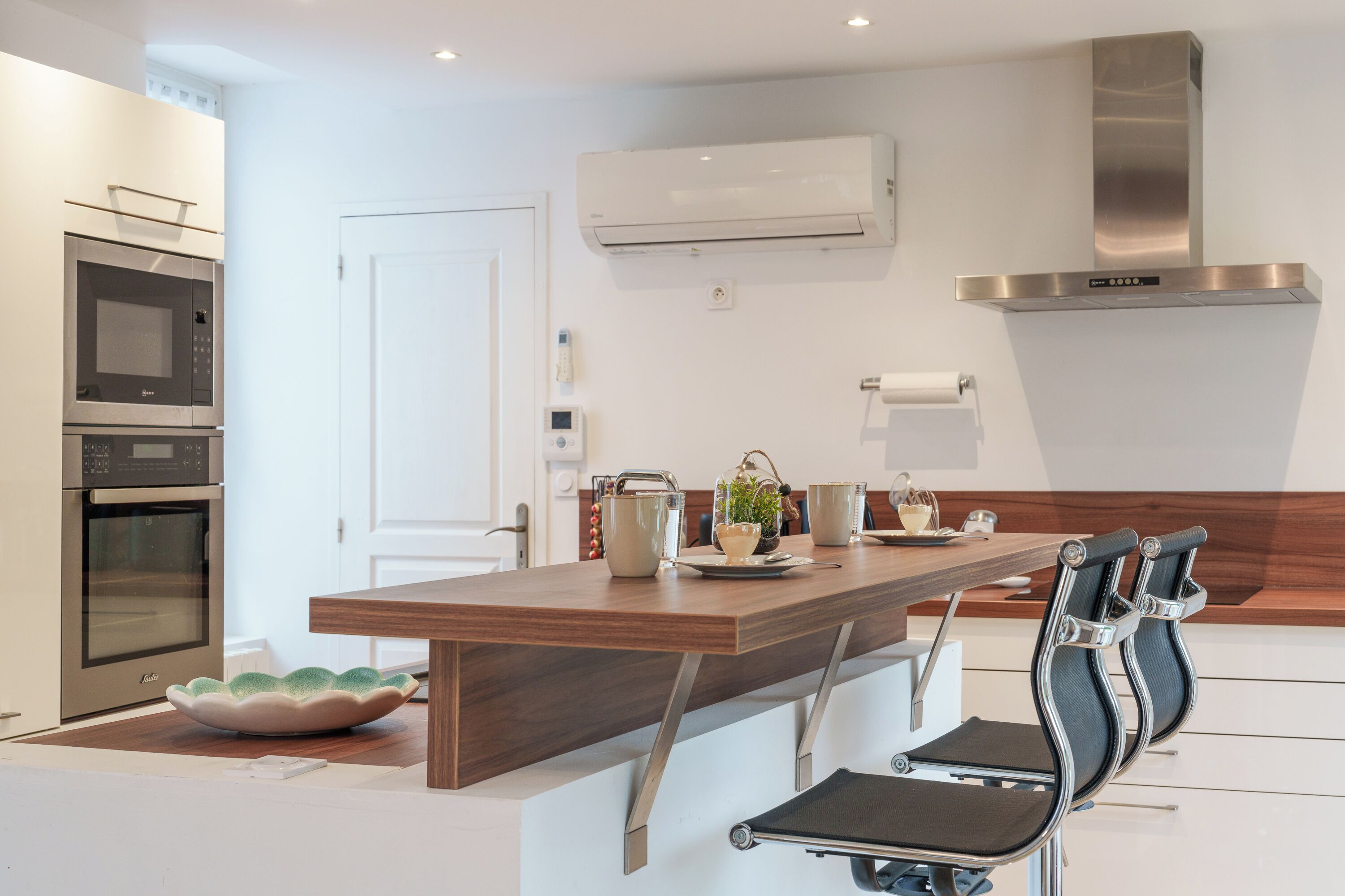 A modern kitchen with built-in appliances, a wooden island, and a seating area with chairs.