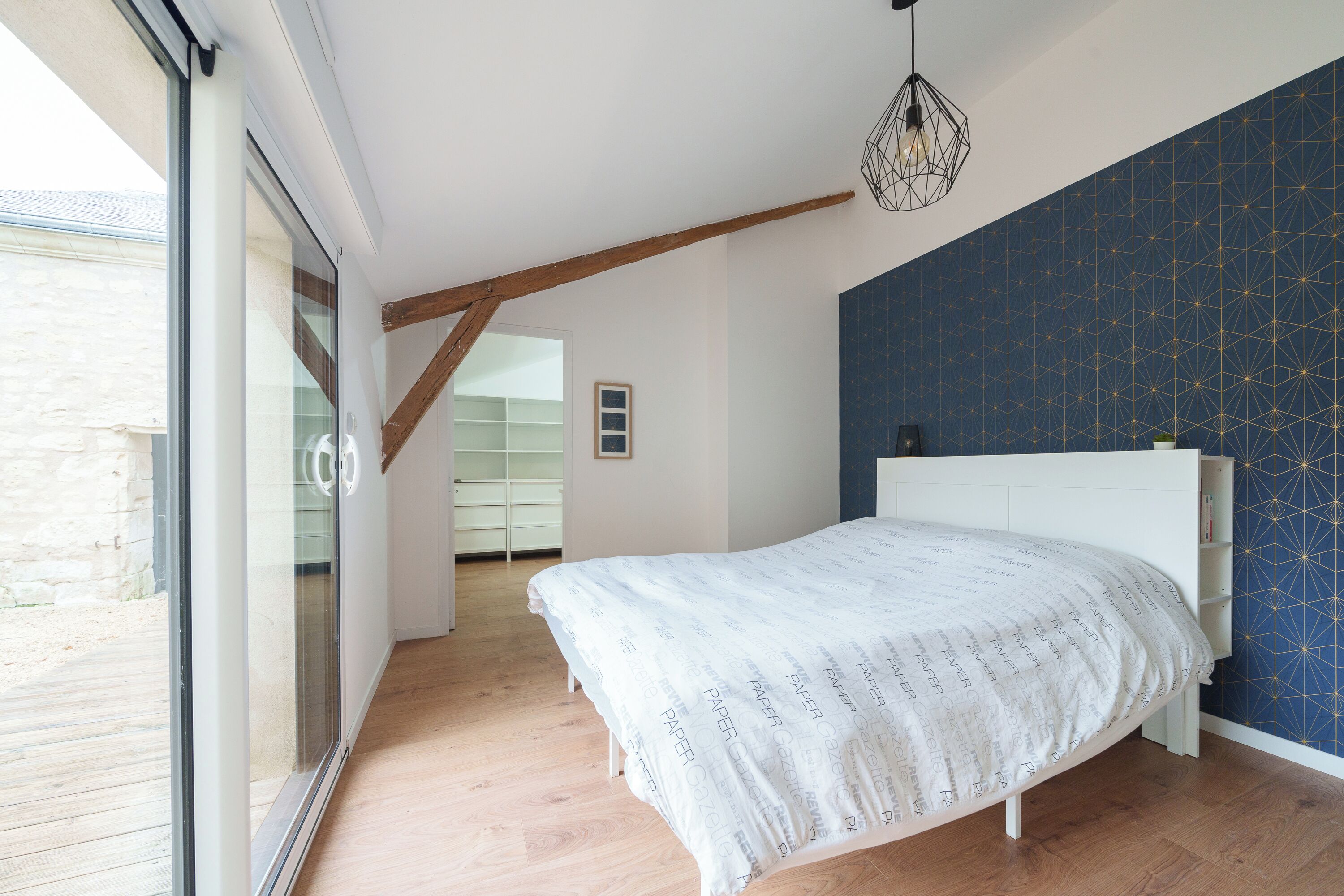 A bedroom with a white bed, wooden floor, and a blue patterned wall.