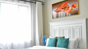 Una camera d'albergo con un letto, un comodino, una sedia, una finestra con tende e un quadro appeso al muro.