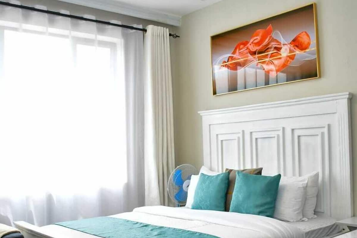 Une chambre d’hôtel avec un lit, une table de chevet, une chaise, une fenêtre avec des rideaux et un tableau au mur.