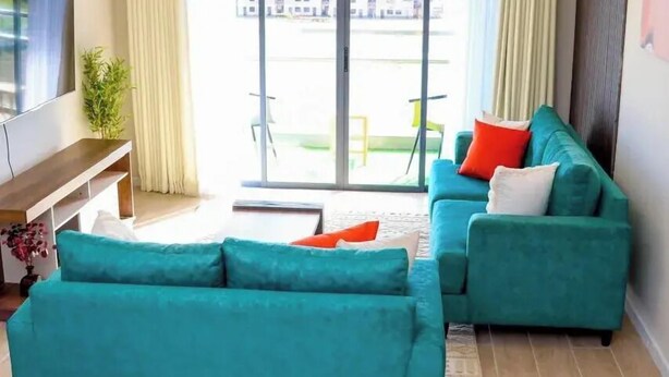Un soggiorno moderno con divani color petrolio, una televisione a schermo piatto e un'ampia porta scorrevole in vetro che dà su una zona esterna.