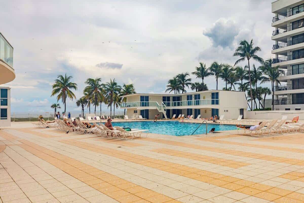 Un espace piscine agrémenté de chaises longues et de palmiers, entouré de bâtiments.