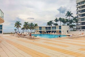 A pool area with lounge chairs and palm trees, surrounded by buildings. - Shine Suites Studio (Miami)