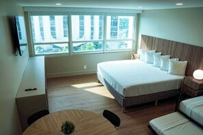 Une chambre d’hôtel moderne, dotée d’un grand lit, d’un bureau, d’une chaise et d’une fenêtre donnant sur des immeubles.