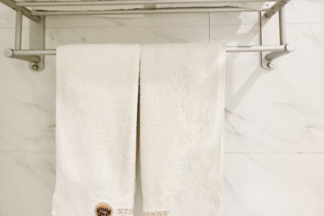 Uma toalha branca pendurada em um porta-toalhas de metal, diante de uma parede de mármore branco.