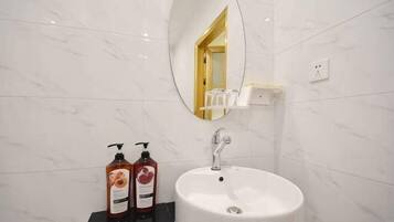 Un baño con un lavamanos blanco, un espejo y dos botellas de champú.