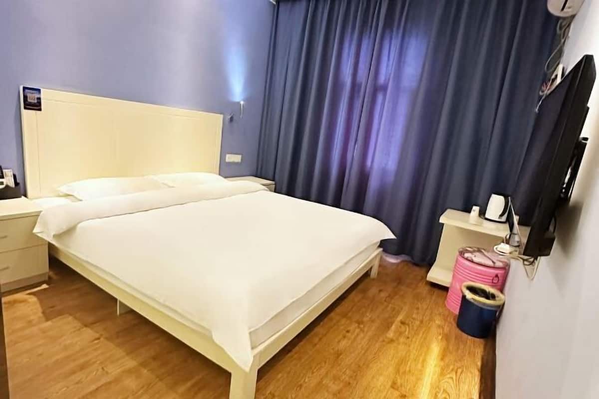 Una habitación de hotel con cama, mesita de noche, televisión y cortina.