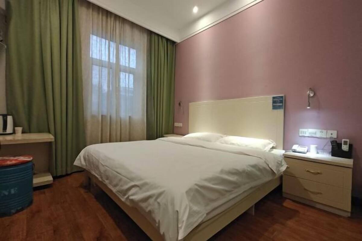 Una habitación de hotel con cama, mesita de noche y ventana con cortinas.