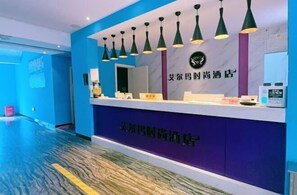 A hotel reception desk with a blue and purple color scheme, a logo above the desk, and a sign with Chinese characters. - Aierma Fashion Hotel (Zhengzhou Zhongyuan Wanda City Center Hospital Subway Station) (Zhengzhou)