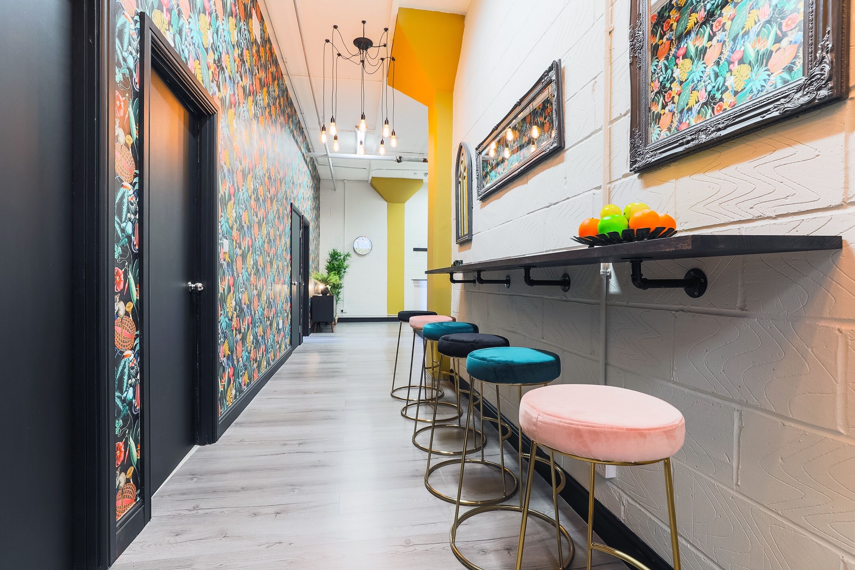 A hallway with colorful patterned walls, a row of bar stools, and a shelf with decorative items.