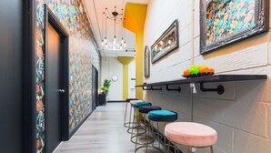 A hallway with colorful patterned walls, a row of bar stools, and a shelf with decorative items.