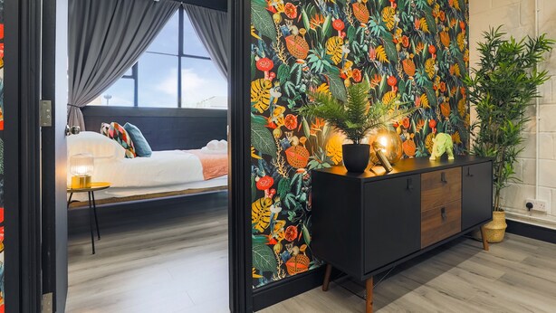 A bedroom with a bed, a nightstand, and a window. There is a black cabinet with decorative items on top.