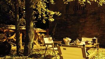 An outdoor seating area with a table set for two, surrounded by chairs, under a tree.