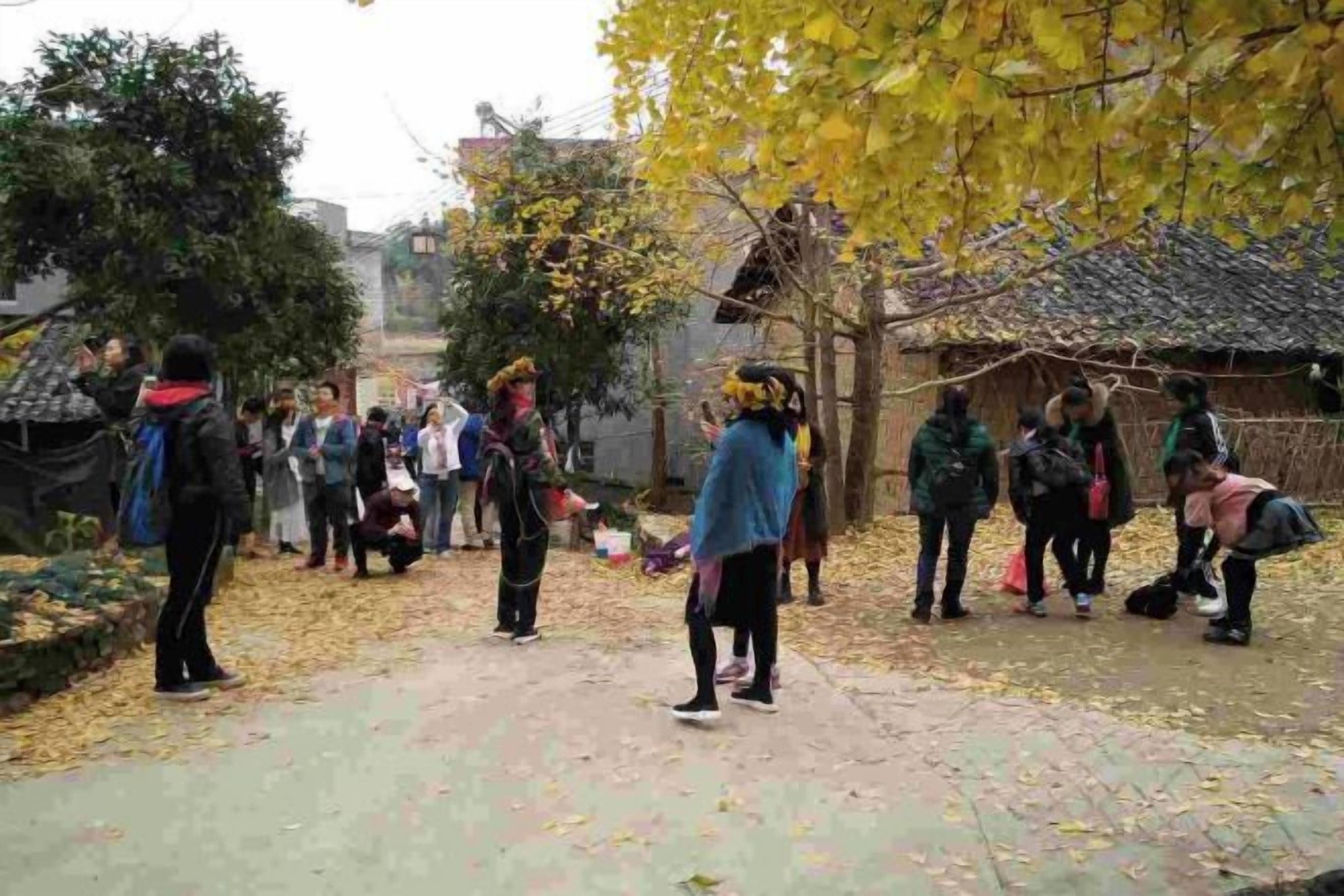 A group of people gathered outdoors, some standing and some crouching, with trees and a building in the background.